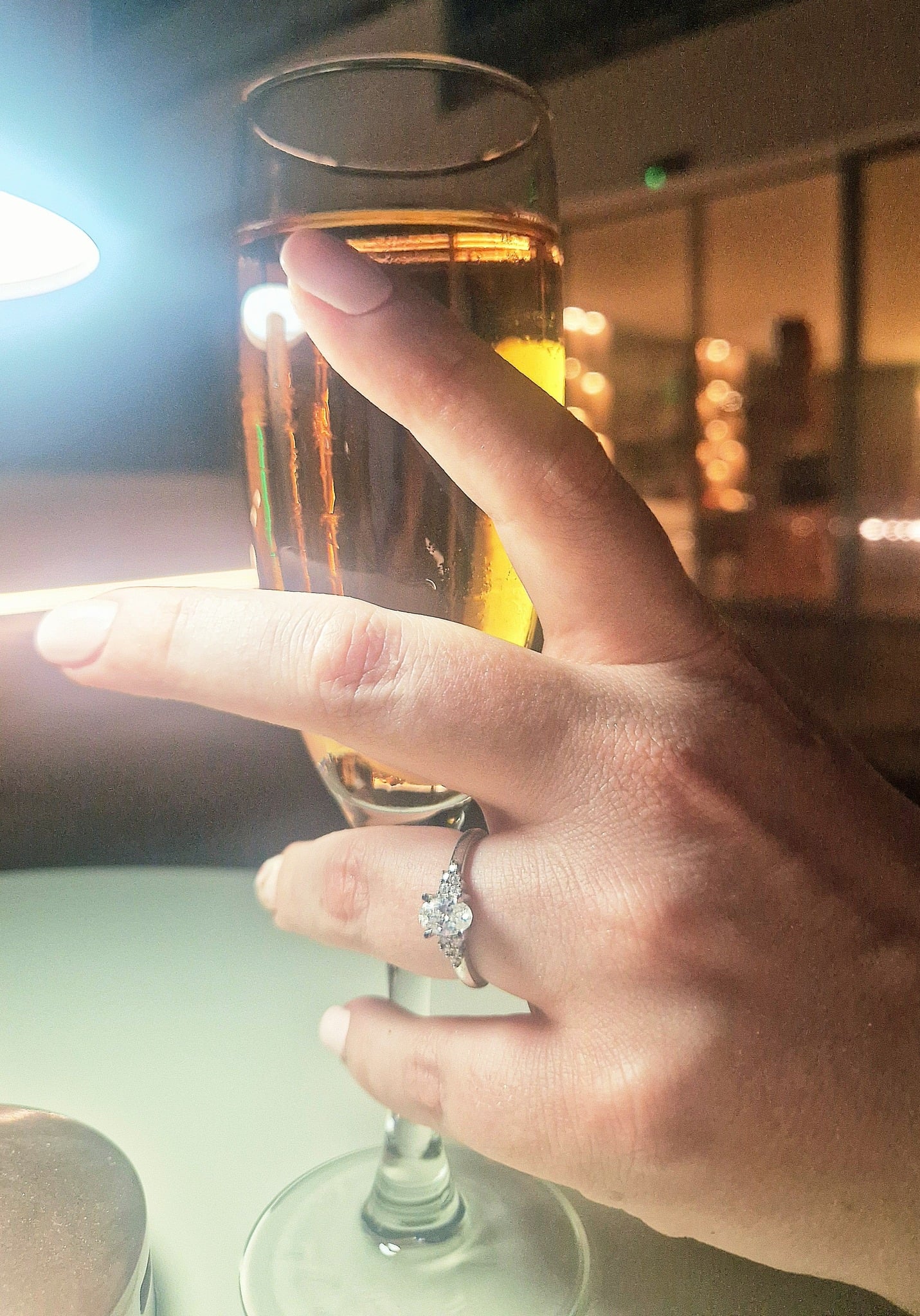 An engagement ring on a finger holding a glass of champagne